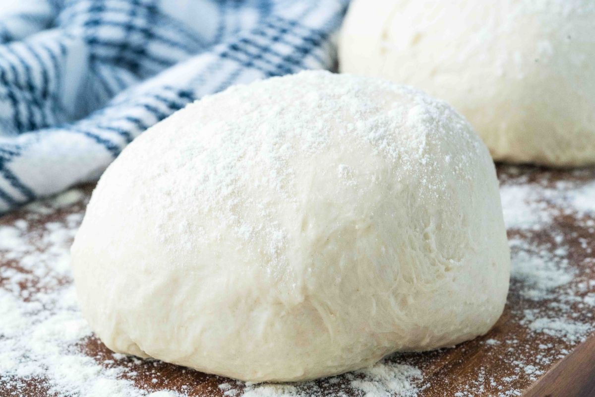 ball of pizza dough covered with flour on wooden board.