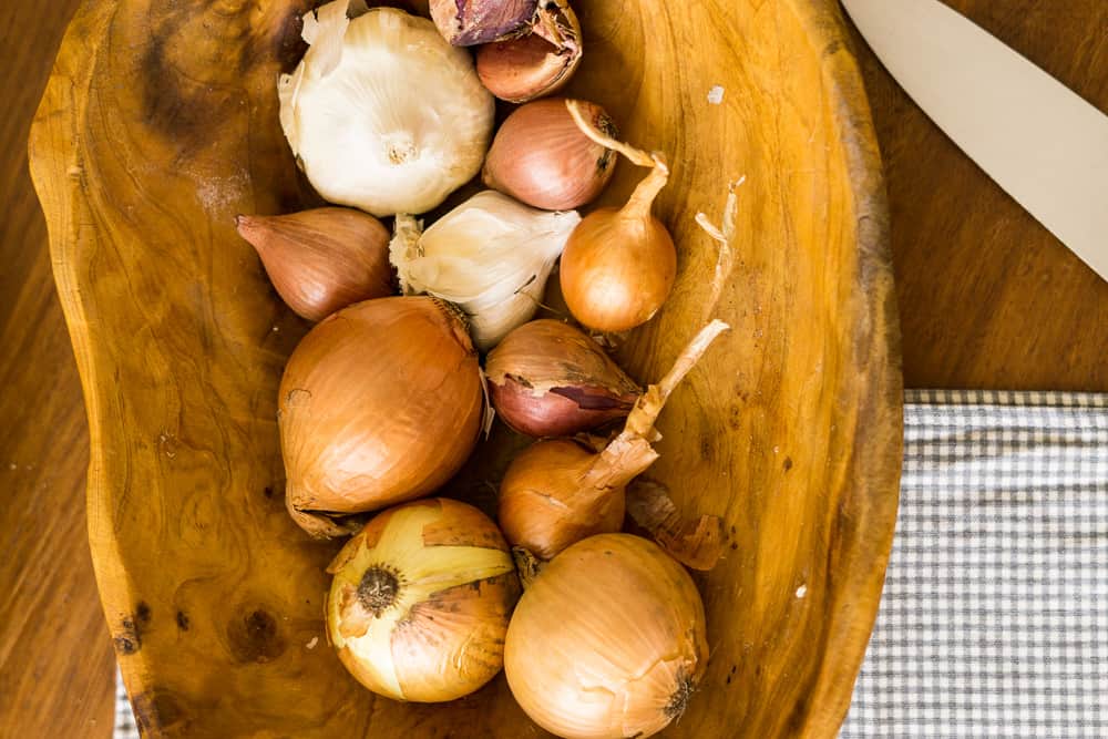 onions and garlic in shallow wooden bowl with large knife and checkered napkin nearby
