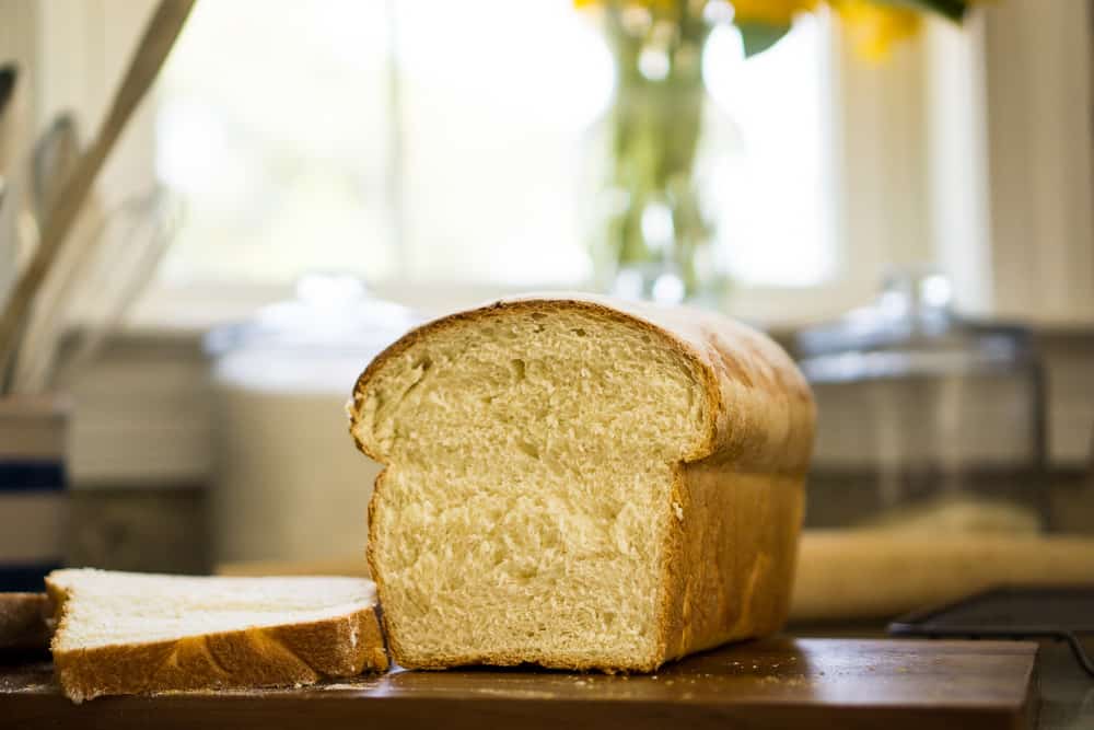 white sandwich loaf with end sliced off, glass jars and wooden rolling in background
