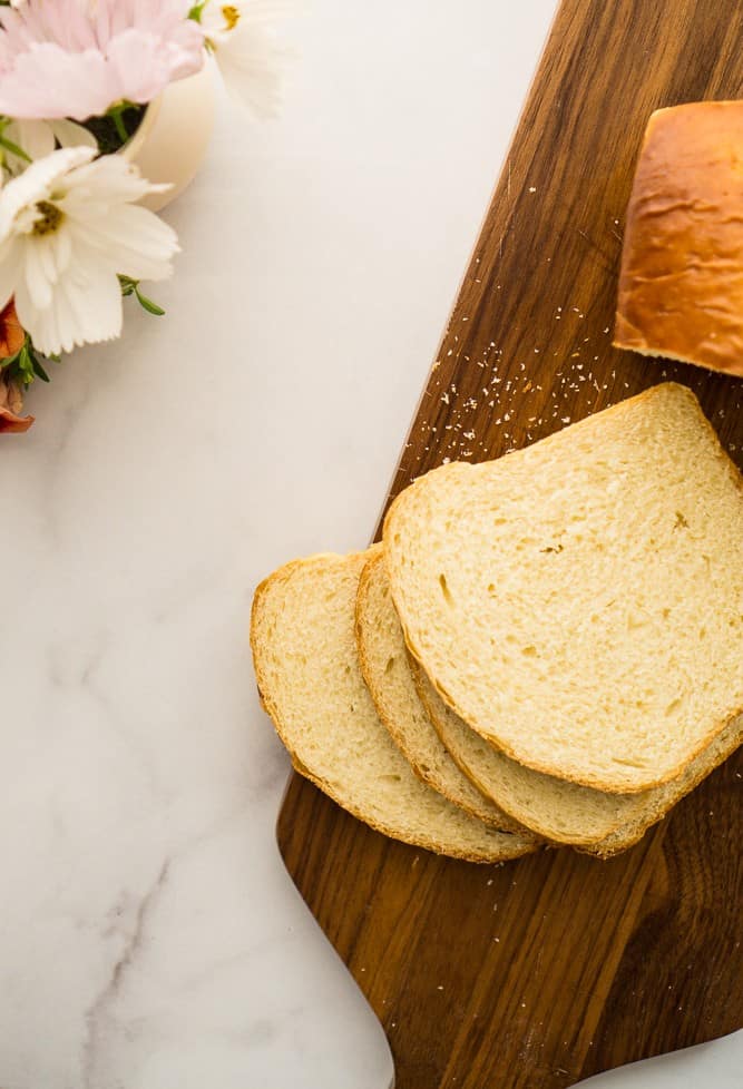 loaf of sweet hawaiian sandwich bread with four slices stacked on cutting board and white and color flowers in upper corner