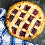 blackberry raspberry pie with lattice top on wooden surface, blue and white plaid tea towel in lower left corner