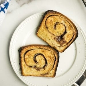 two slices cinnamon swirl sourdough bread, toasted and buttered, on white plate on marble counter