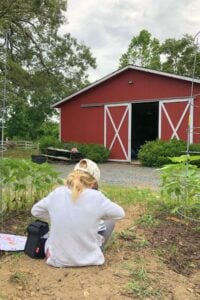 girl drawing in garden in front of barn