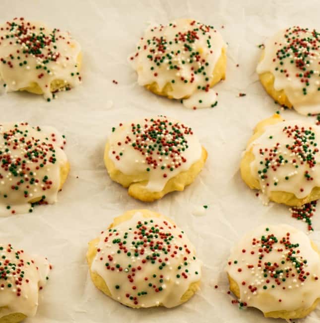 9 sour cream cookies on parchment paper with white glaze and christmas sprinkles