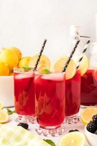 three glasses of blackberry lemonade with black straws.