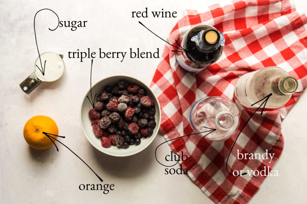concrete surface with mixed berries, orange, red wine, sugar, vodka, and club soda