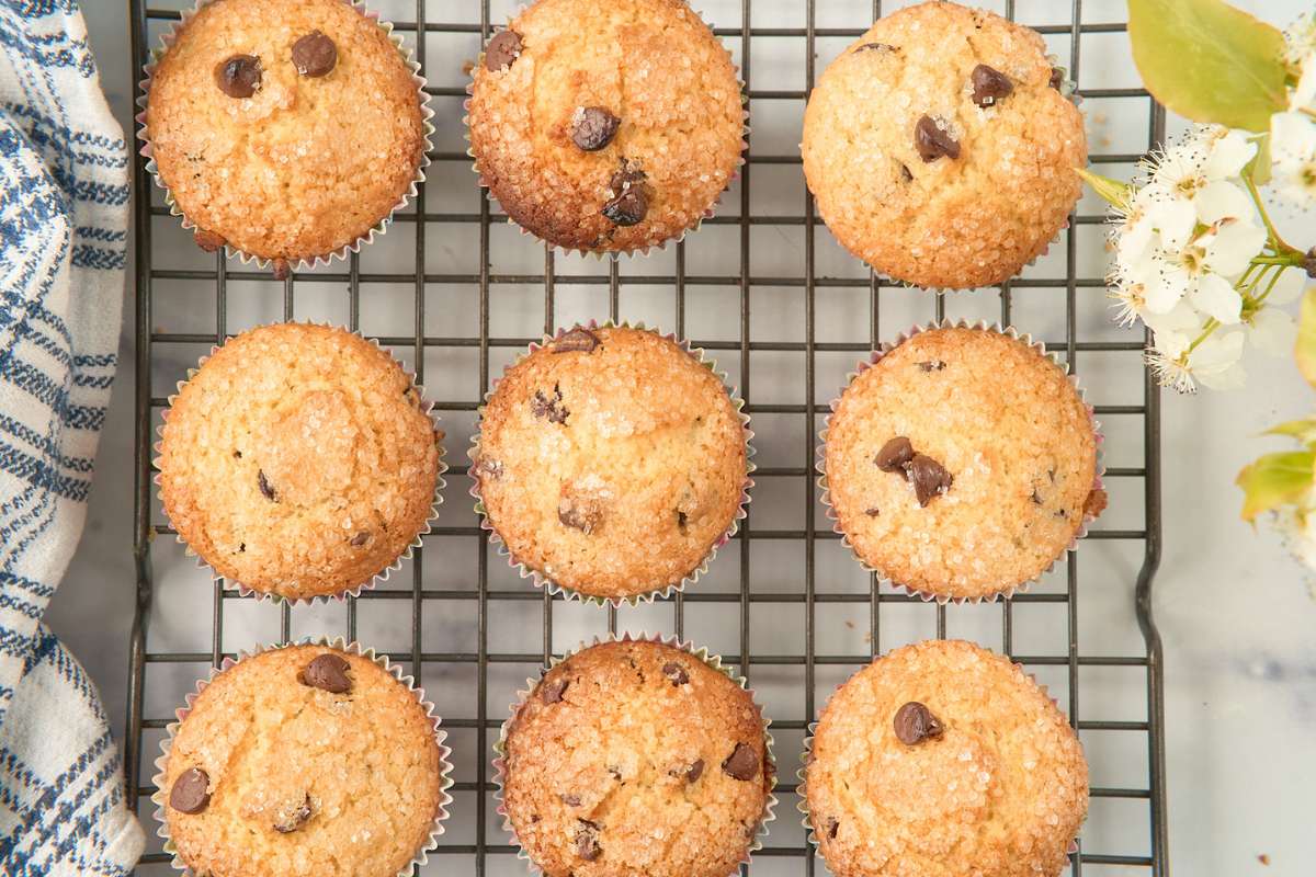 Nine muffins cooling on a wire rack next to flowers.