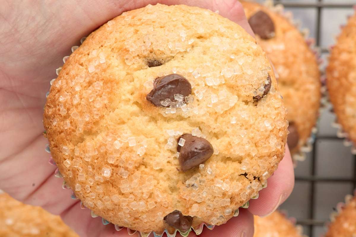 Hand holding a muffin topped with sugar and chocolate chips.