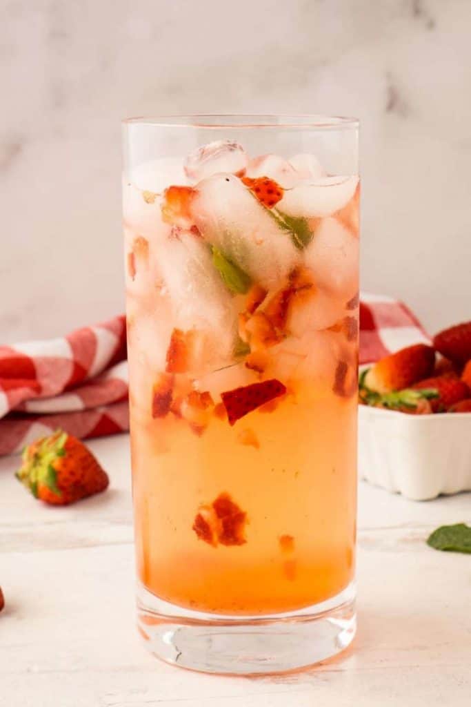 cocktail glass with ice, fresh strawberries, mint, and drink