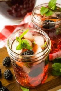2 mason jars filled with blackberry tea on ice with fresh mint and berries