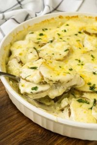spoon lifting cheesy scalloped potatoes out of dish.