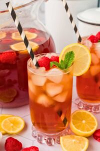 raspberry peach sweet tea in glasses and pitcher with straws and lemon wedges.