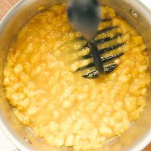 peaches and sugar being mashed in saucepan