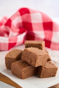 pieces of fudge stacked on plate with red checkered cloth in background.