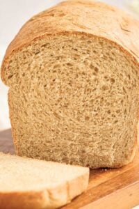 sliced loaf of honey wheat sandwich bread on cutting board.