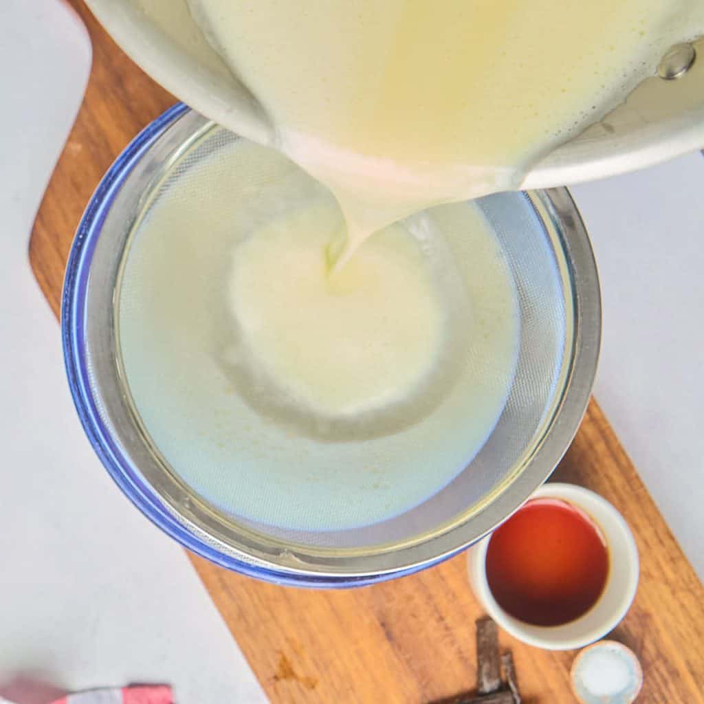 straining custard over glass bowl