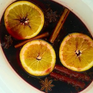 slow cooker filled with wine topped with orange slices and cinnamon sticks