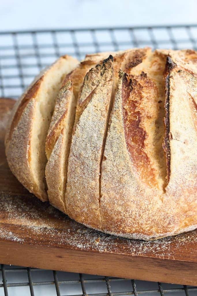 loaf of sourdough bread on cooling rack being sliced