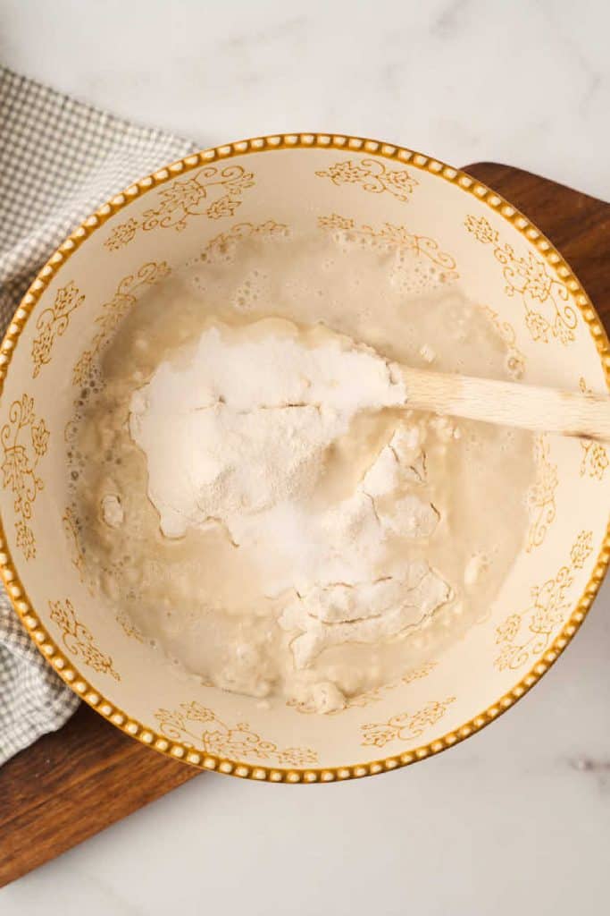 mixing bowl with sourdough starter, flour and salt with wooden spoon on top