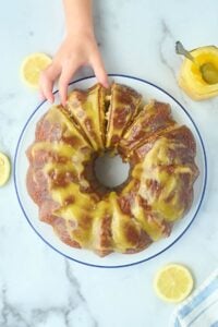 bundt cake with lemon slices next to it and hand reaching for a piece