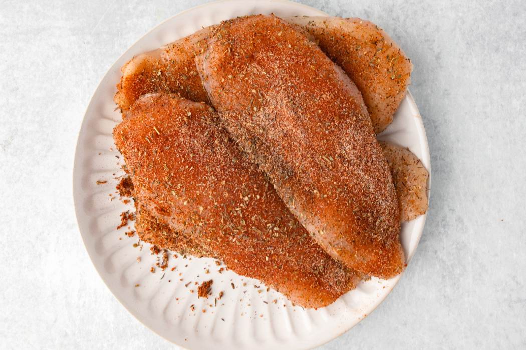 seasoned chicken breast on plate before cooking.
