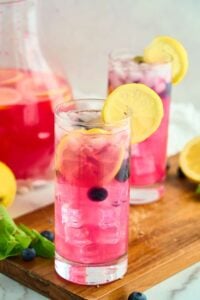 2 glasses and pitcher of pink drink on wooden board