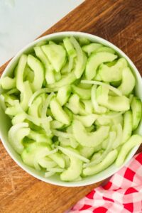 white bowl filled with peeled cucumbers and sliced onion
