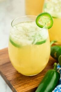 glass of yellow sangria next to fresh jalapeno peppers