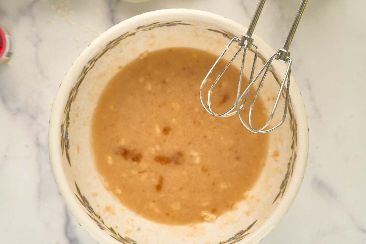 Bowl of blended banana, sugar, and oil with beaters resting on the edge.