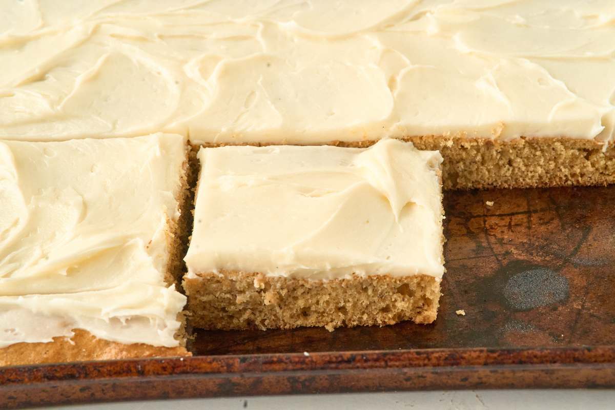 Banana cake cut into squares and frosted with cream cheese icing in baking pan.