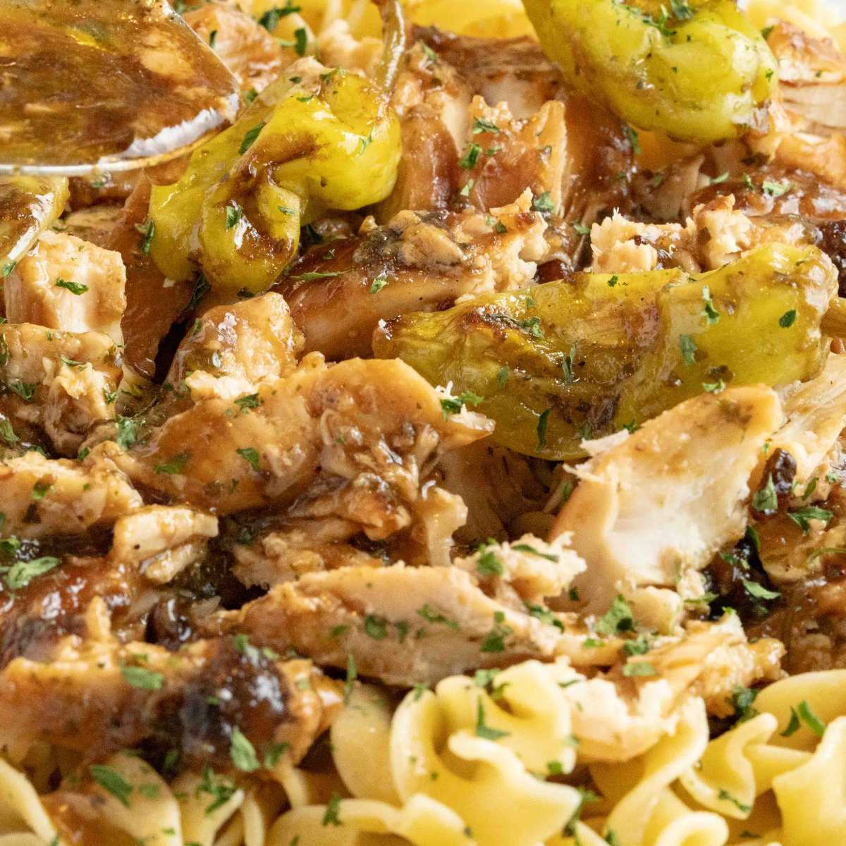 close up of Mississippi chicken with peppers over noodles.