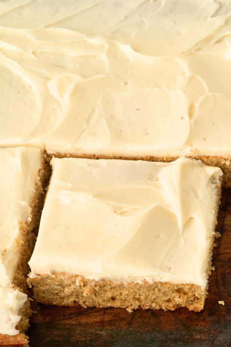 Close-up of banana cake topped with frosting, cut into squares in a jelly roll pan.
