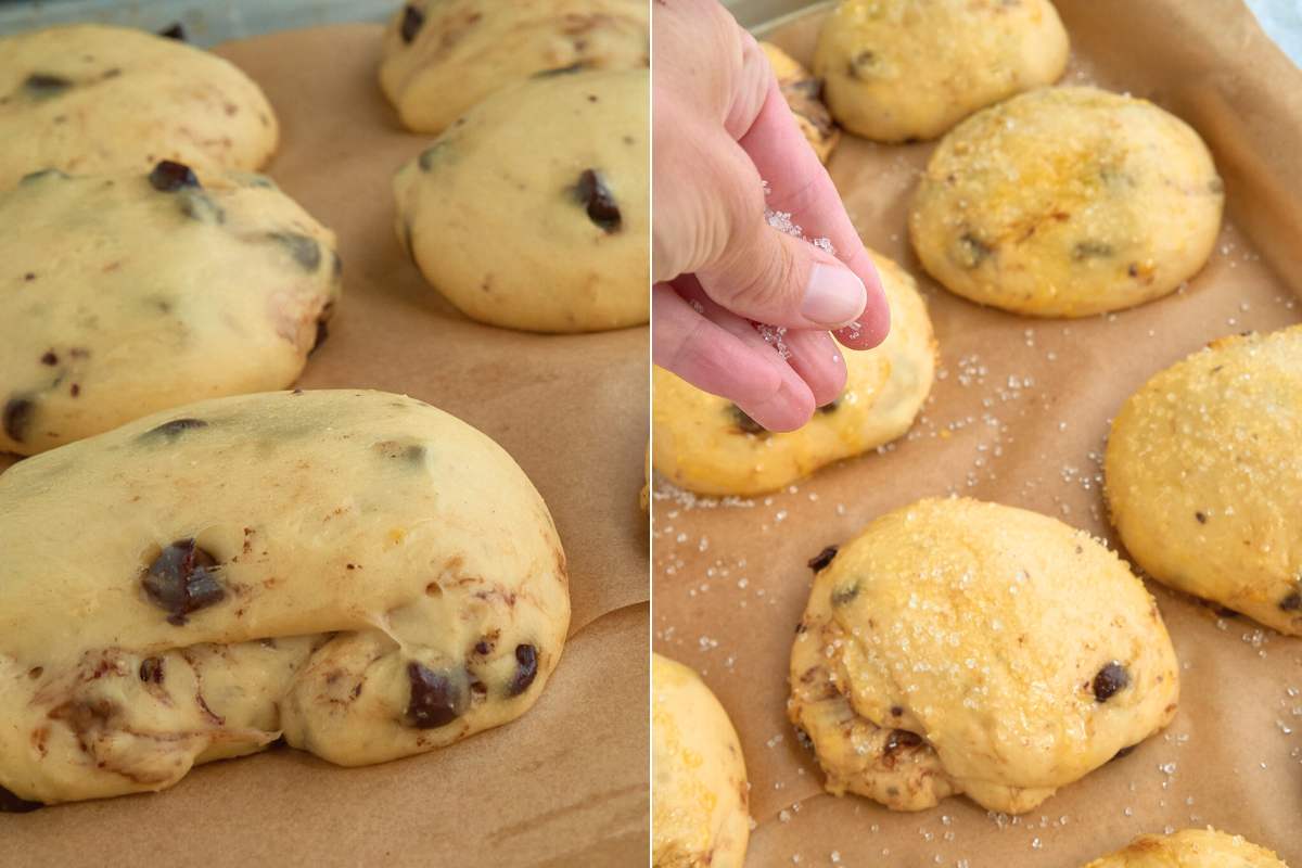 Hand sprinkling sugar on unbaked chocolate chip rolls on a tray.