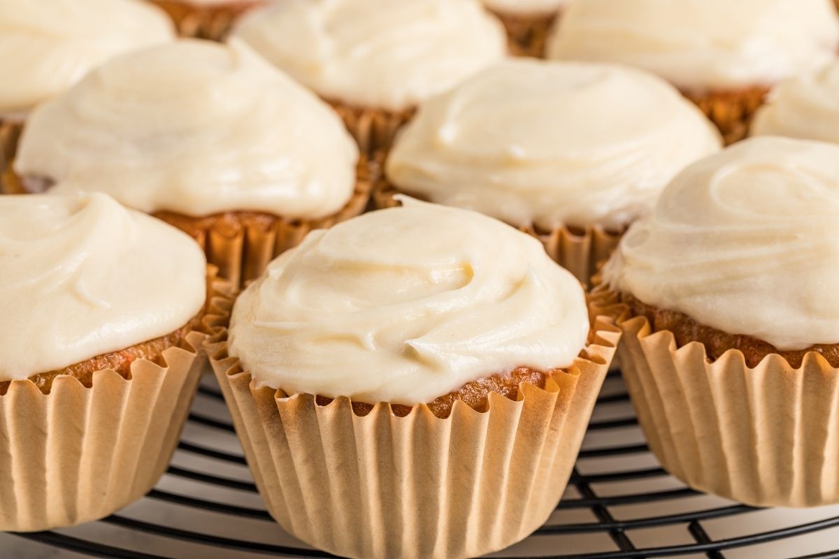 Frosted carrot cupcakes in brown paper liners on a wire cooling rack.