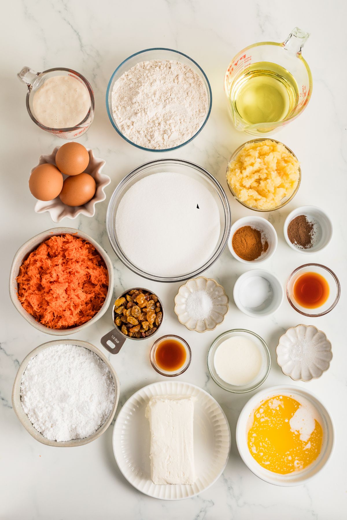 All ingredients for carrot cupcakes and frosting measured in small bowls.