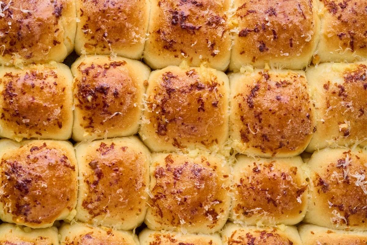 Rows of golden garlic parmesan dinner rolls in a rectangular baking pan.
