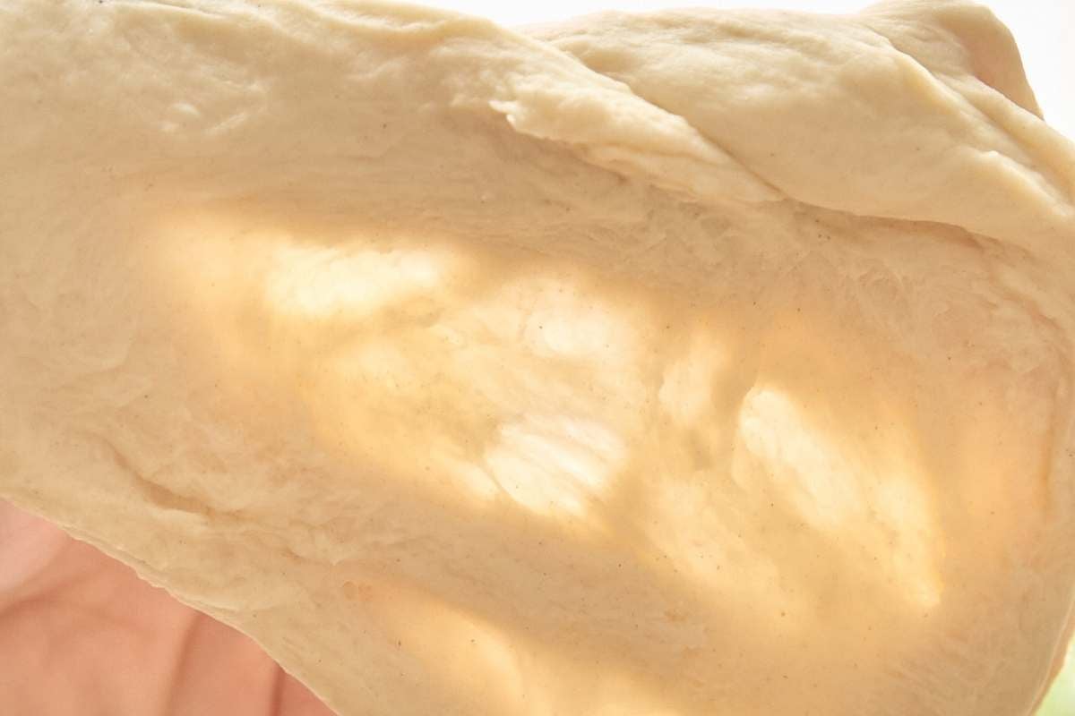 Hands stretching bread dough thin enough to see through for windowpane test.