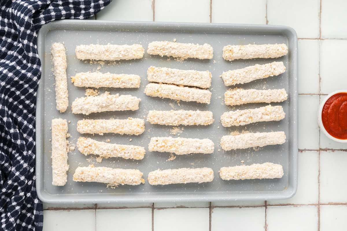 breaded mozzarella sticks on baking sheet for freezing.
