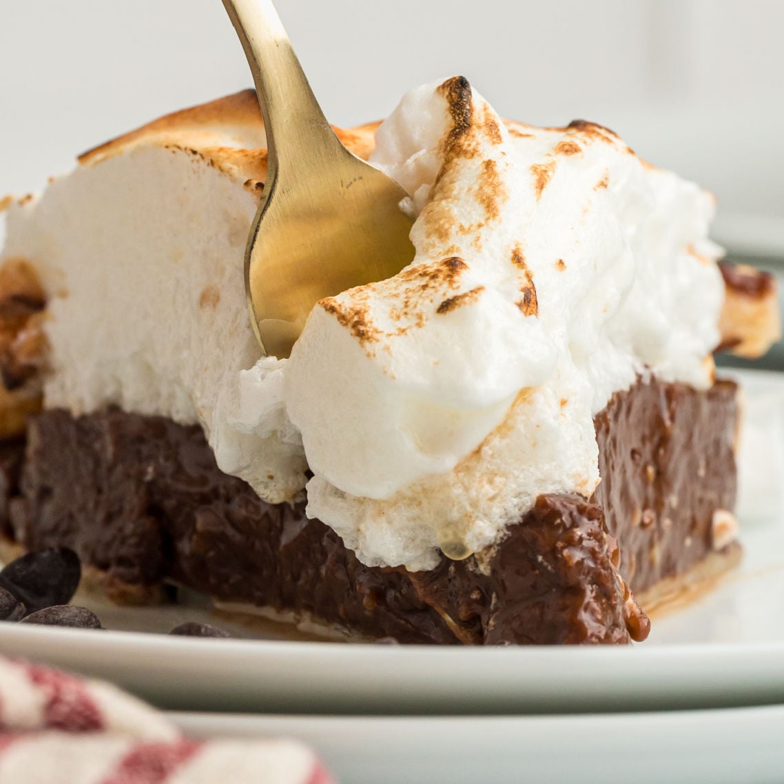 piece of chocolate meringue pie with gold fork inserted.