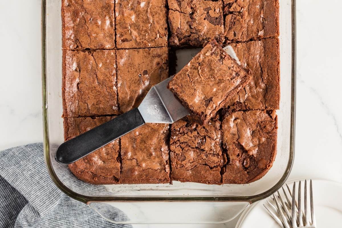 Brownies in a glass pan with one being lifted out by a spatula.