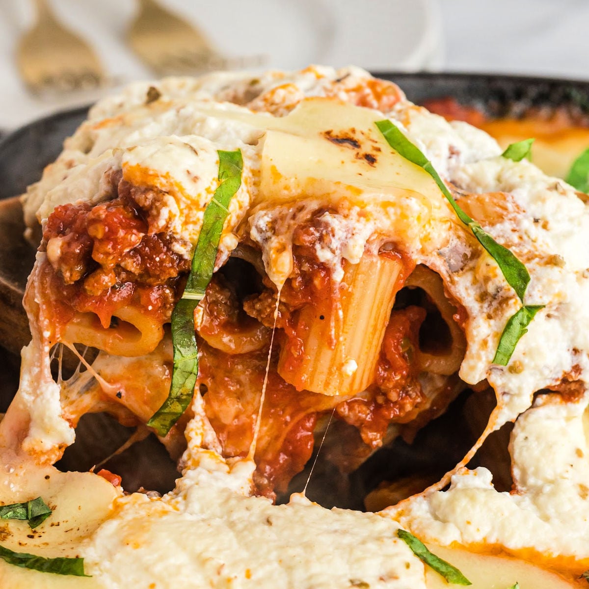 close up of scoop of rigatoni pasta with cheesy layer on top.