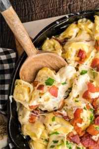 skillet with tortellini topped with cheese and white sauce.