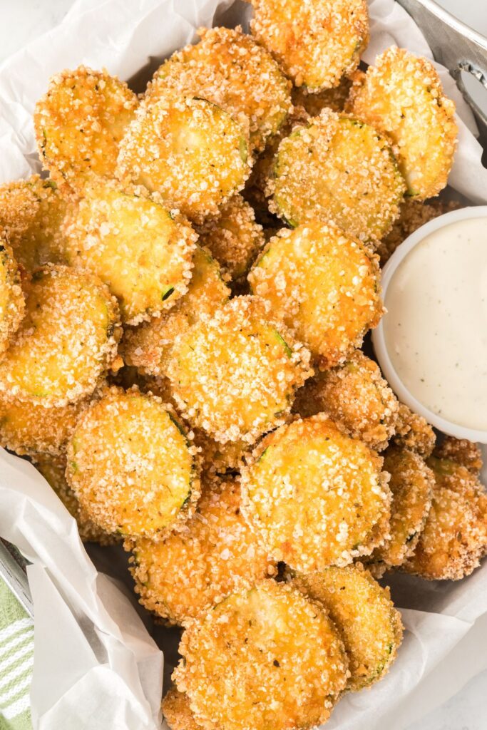 container of round slices of fried zucchini. with. ranch on side.