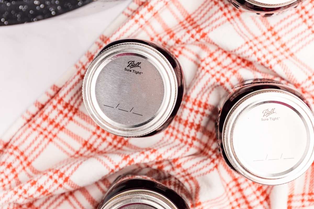 Sealed jars of blueberry pie filling cooling on a checkered cloth.