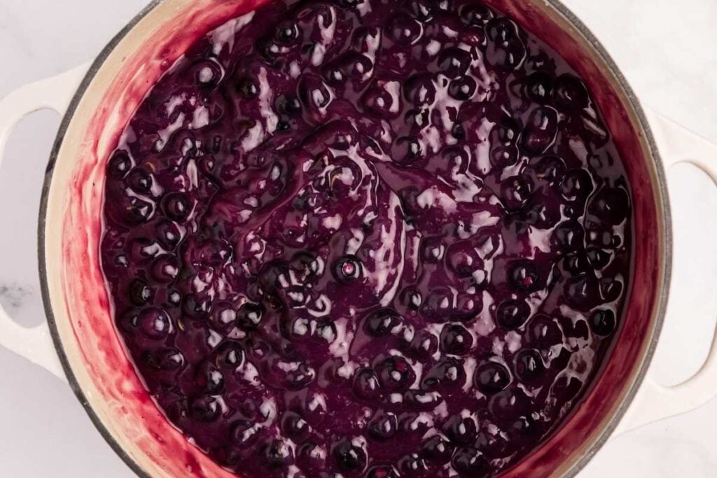 Whole blueberries folded into thick purple filling in a pot.