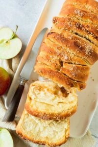 top view of apple pie yeast bread sliced with knife and apples on the side.