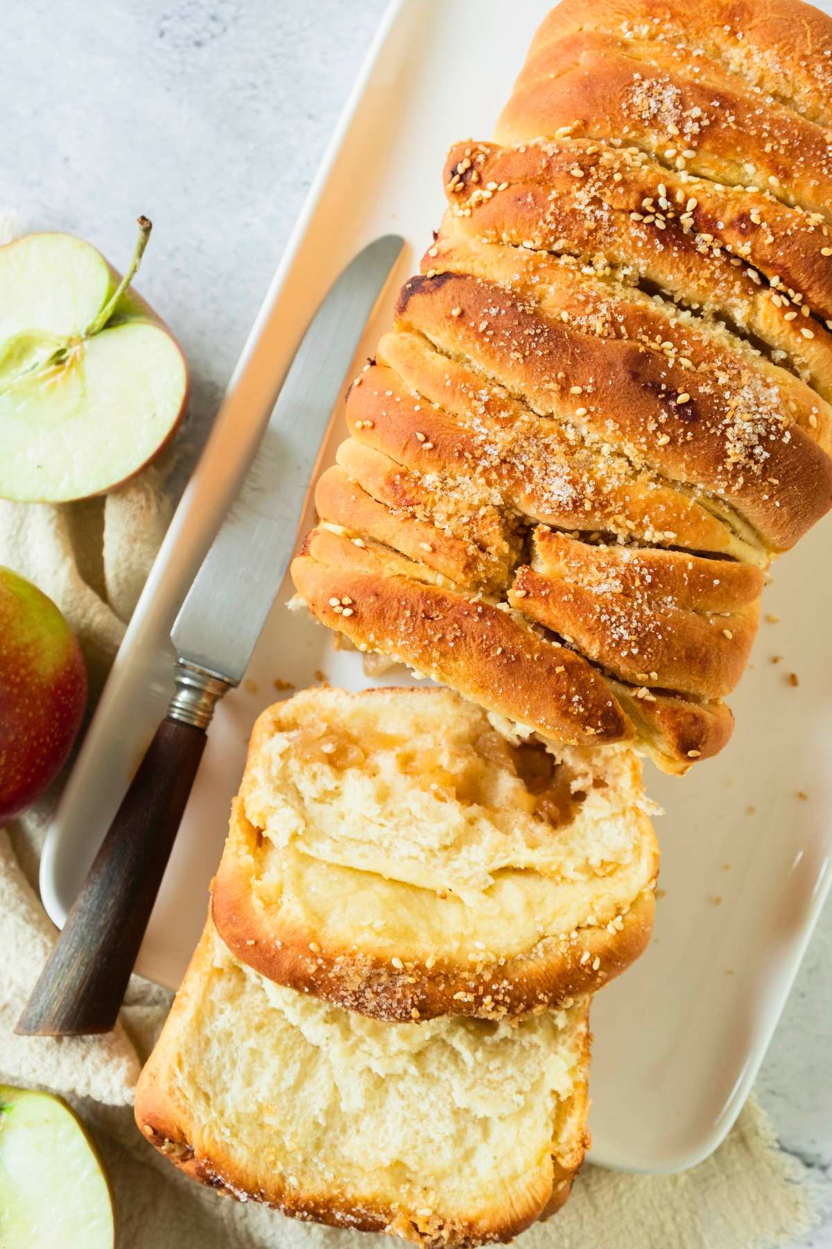 top view of apple pie yeast bread sliced with knife and apples on the side.