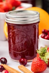 jar of canned christmas jam surrounded by berries and orange.