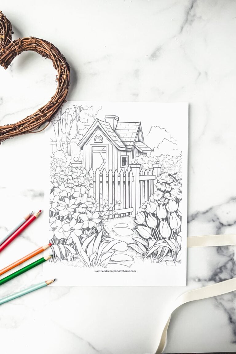cottage coloring page on white marble with colored pencils and twine wreath nearby.