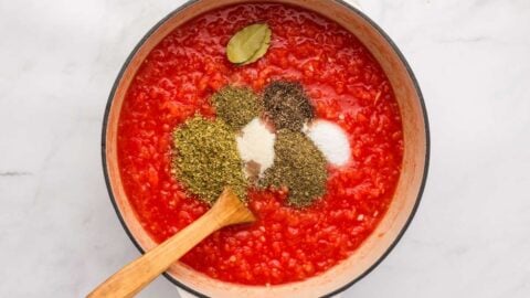 spices and sugar being added to crushed tomatoes.